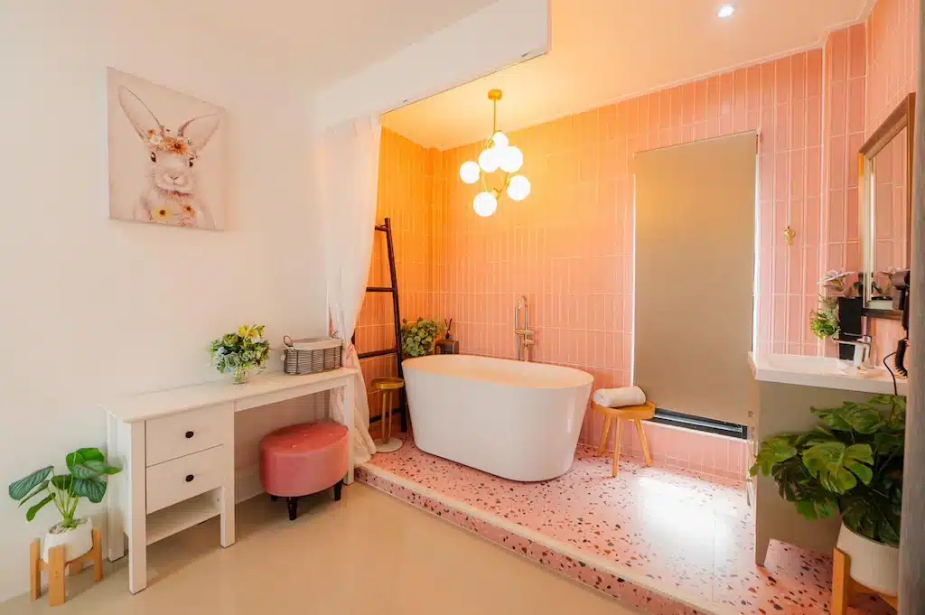 ห้องน้ำสไตล์โมเดิร์นพร้อมอ่างอาบน้ำแบบลอยตัว ผนังกระเบื้องสีชมพู เคาน์เตอร์ล้างหน้าสีขาว ต้นไม้ในกระถาง และงานศิลปะรูปกระต่าย—เหมาะสำหรับการผ่อนคลายหลังจากสำรวจ เกาะล้านที่พัก หรือค้นหา ที่พักเกาะล้านราคาถูก ที่คุณชื่นชอบ.