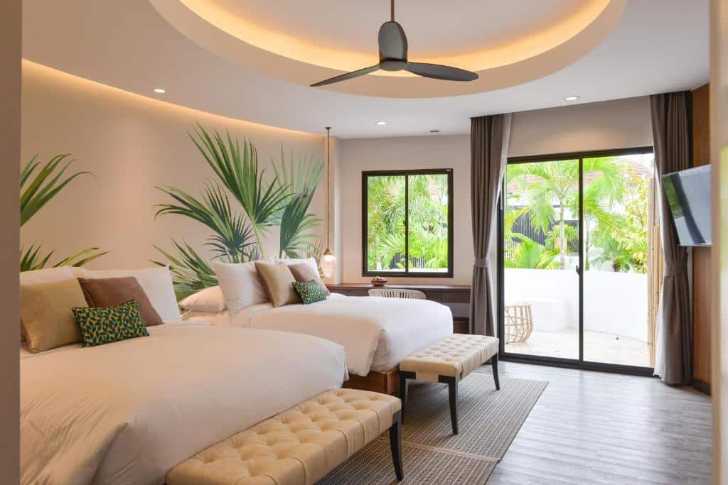 ห้องพักโรงแรมสมัยใหม่พร้อมเตียงขนาดใหญ่สองเตียง, ม้านั่ง, ภาพจิตรกรรมฝาผนังแบบเขตร้อน, พัดลมเพดาน, โทรทัศน์ติดผนัง, และประตูบานเลื่อนเปิดออกสู่ระเบียงที่มีต้นไม้เขียวชอุ่ม—ที่พักประจวบคีรีขันธ์ที่สมบูรณ์แบบสำหรับการเข้าพักครั้งต่อไปของคุณที่โรงแรมสไตล์ทันสมัยในประจวบ.