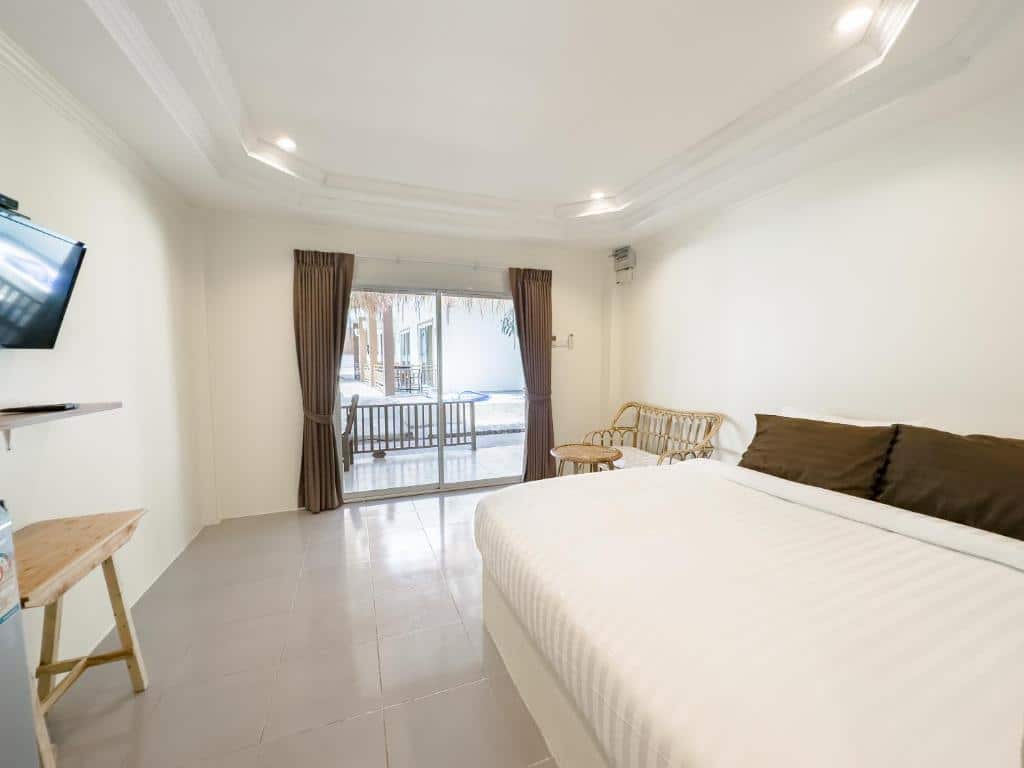 ห้องพักโรงแรมขนาดเล็กที่มีเตียงขนาดใหญ่, หมอนสีน้ำตาล, โต๊ะเล็ก, โทรทัศน์ติดผนัง, และประตูบานเลื่อนกระจกที่เปิดออกสู่ทัศนียภาพของสระว่ายน้ำ—เหมาะสำหรับการพักผ่อนของคุณที่ ที่พักเกาะล้านติดทะเล.