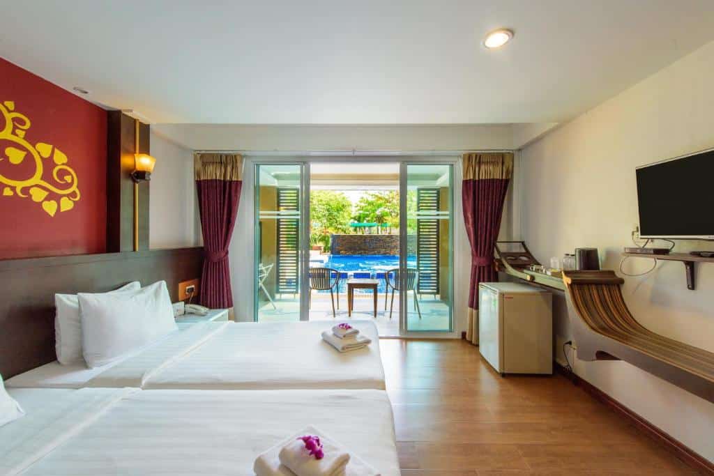 ห้องพักโรงแรมพร้อมเตียงสองเตียง โทรทัศน์จอแบน ตู้เย็นขนาดเล็ก และประตูกระจกบานเลื่อนเปิดออกสู่ระเบียงพร้อมวิวสระว่ายน้ำ ที่ โรงแรมประจวบ—ที่พักประจวบคีรีขันธ์ที่สมบูรณ์แบบสำหรับการพักผ่อนใกล้ทะเล.