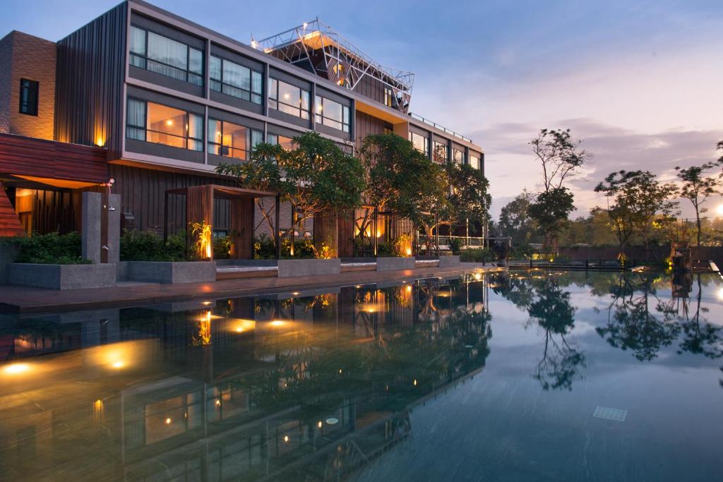 โรงแรมสมัยใหม่ที่มีหน้าต่างบานใหญ่สะท้อนในสระว่ายน้ำกลางแจ้งยามพลบค่ำ ล้อมรอบด้วยต้นไม้และแสงไฟอบอุ่น—เหมาะสำหรับผู้ที่มองหาที่พักเชียงใหม่ท่ามกลางธรรมชาติในบรรยากาศเงียบสงบ.