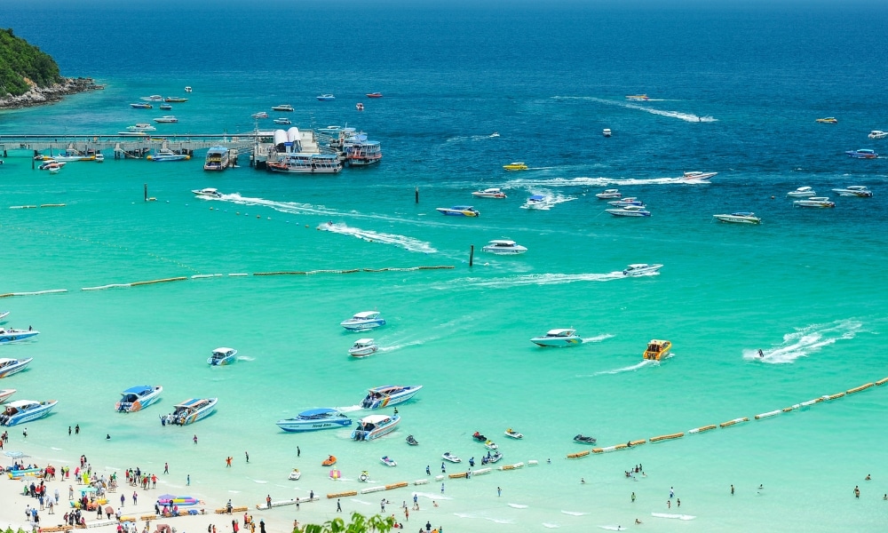 ชายหาดที่แออัดด้วยผู้คน น้ำทะเลสีฟ้าเทอร์ควอยซ์ มากมายไปด้วยผู้คน และเรือเร็วรวมถึงเรือต่างๆ มากมายในทะเลใกล้ท่าเรือ เหมาะสำหรับผู้ที่ต้องการที่พักเกาะล้านติดทะเล หรือที่พักเกาะล้านใกล้ชายฝั่งที่มีชีวิตชีวา.