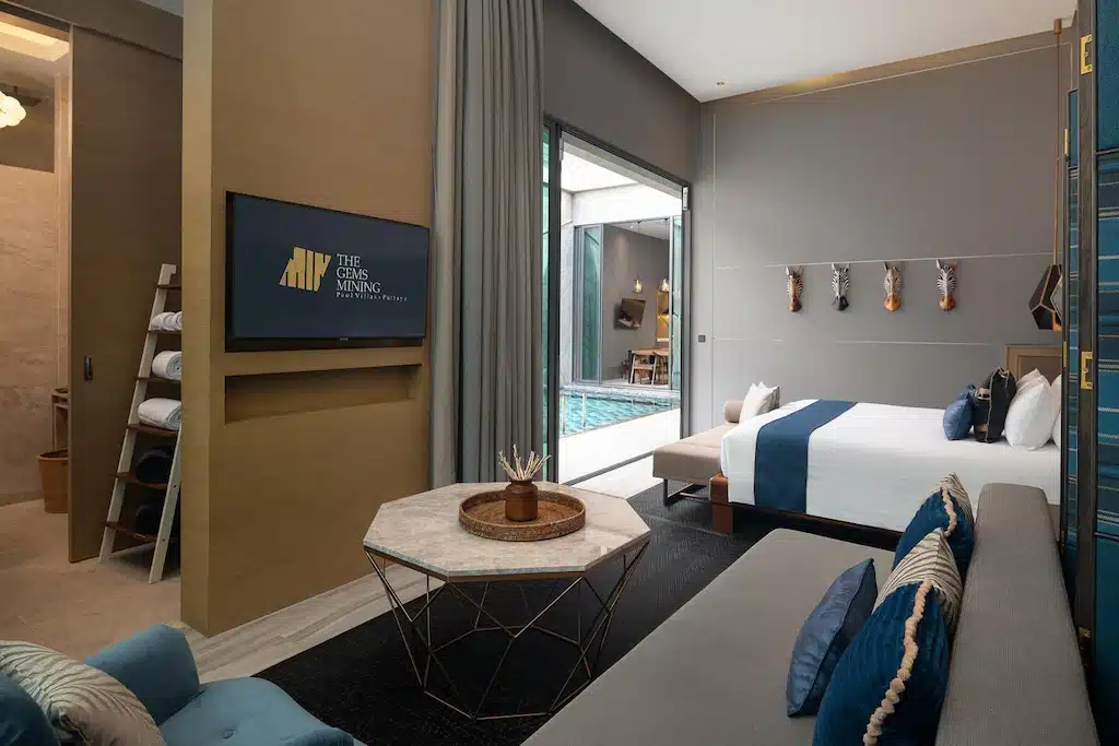 ห้องพักโรงแรมสมัยใหม่พร้อมเตียง โซฟา โทรทัศน์ติดผนัง และประตูกระจกบานเลื่อนเปิดออกสู่สระว่ายน้ำส่วนตัว การตกแต่งเน้นโทนสีเรียบพร้อมรายละเอียดสีฟ้า เหมาะสำหรับการพักผ่อนที่ พูลวิลล่าพัทยาติดทะเล.