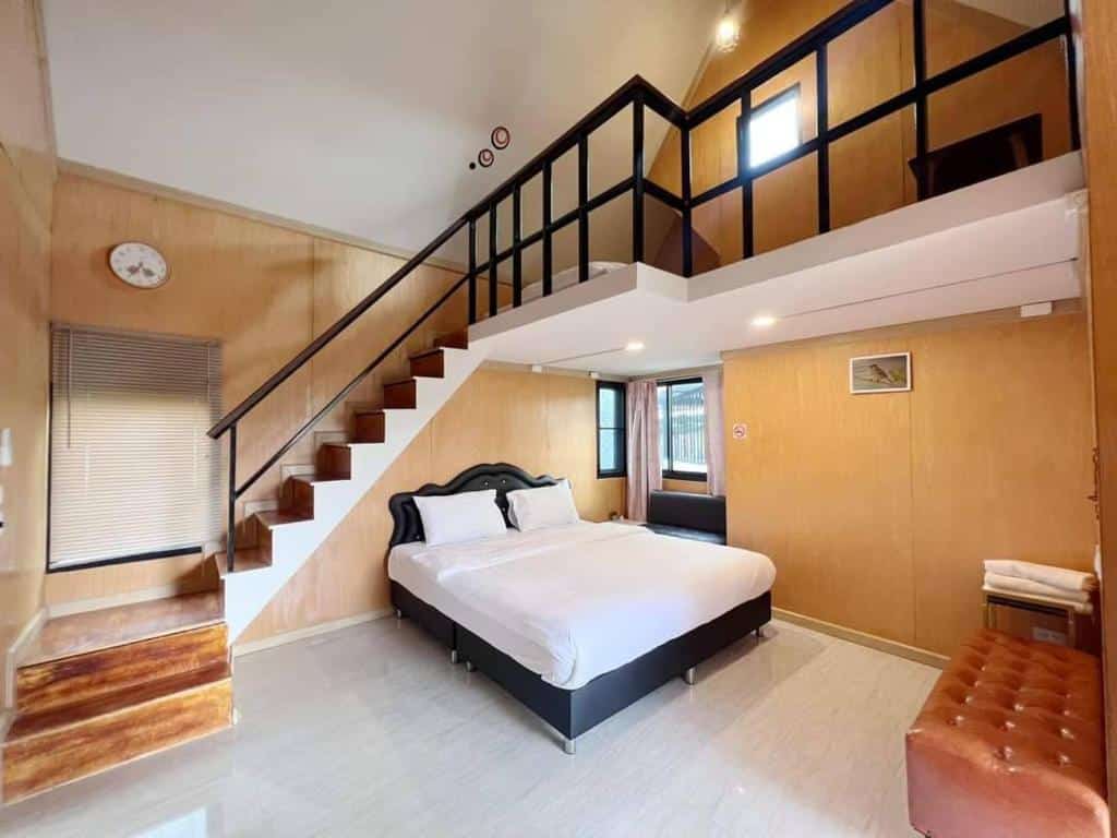ห้องนอนสไตล์โมเดิร์นในพูลวิลล่าเขาค้อ พร้อมเตียงคู่ ผนังไม้ พื้นที่ลอฟท์ที่สามารถเข้าถึงได้ทางบันได หน้าต่าง นาฬิกา และเฟอร์นิเจอร์น้อยชิ้น.