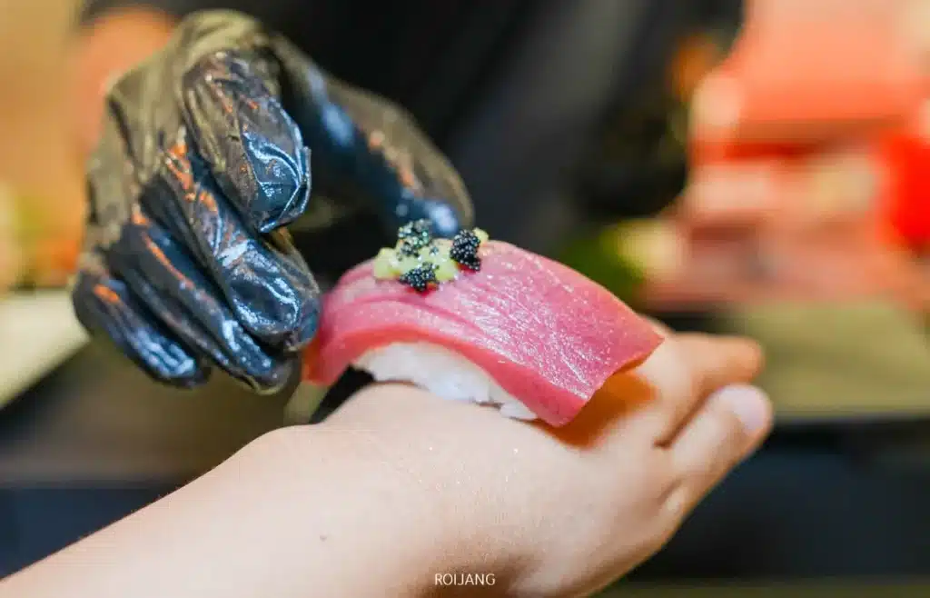 มือที่สวมถุงมือวางซูชิปลาทูน่าชิ้นหนึ่งพร้อมเครื่องเคียงลงบนฝ่ามือของอีกคนหนึ่ง สะท้อนความสง่างามอันเงียบสงบของหุบเขาหมอก.