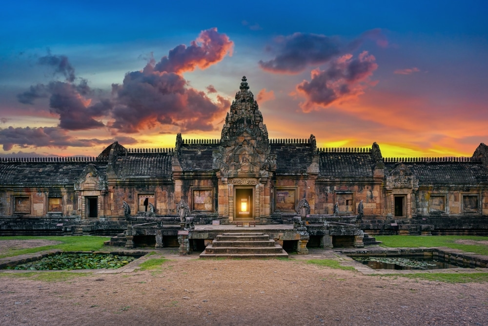 วัดหินโบราณพร้อมลวดลายแกะสลักอันประณีตในยามพระอาทิตย์ตกดิน ประตูทางเข้าหลักส่องประกายอยู่ใต้เมฆที่งดงาม—สถานที่ที่ไม่ควรพลาดสำหรับผู้ที่มองหา ที่เที่ยวบุรีรัมย์.