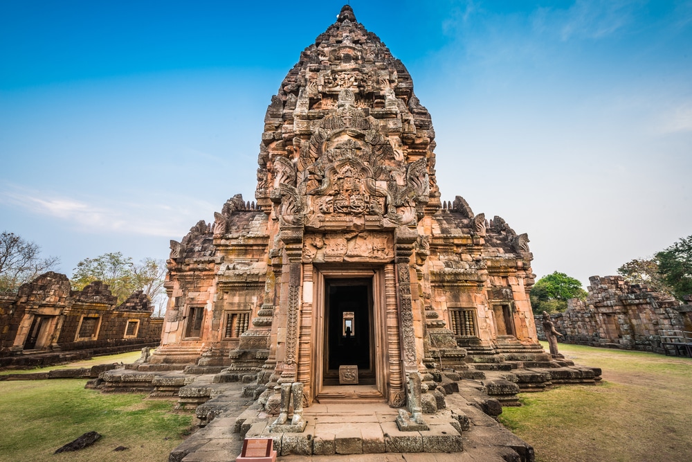 วัดหินโบราณที่มีลวดลายแกะสลักอันประณีตและยอดแหลมสูงตรงกลาง ล้อมรอบด้วยสนามหญ้าภายใต้ท้องฟ้าสีคราม—หนึ่งในสถานที่ท่องเที่ยวบุรีรัมย์ที่ต้องไปเยือนสำหรับผู้หลงใหลในประวัติศาสตร์.