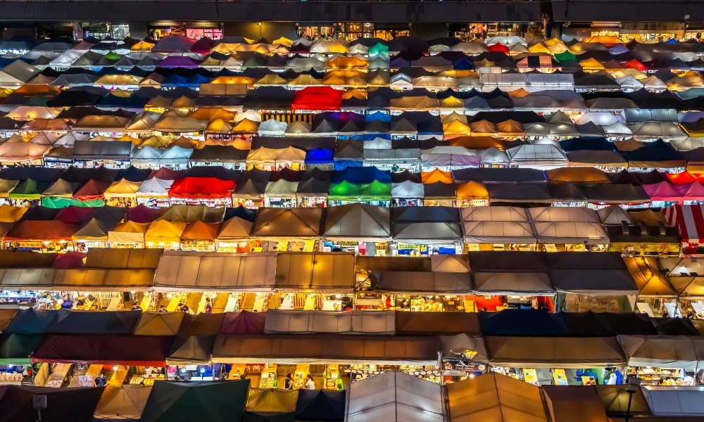ภาพมุมสูงของตลาดกลางคืน หนึ่งในสถานที่ท่องเที่ยวที่ดีที่สุดในกรุงเทพฯ มีแผงขายของสีสันสดใสเรียงรายเป็นตาราง.