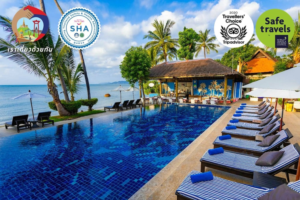 พื้นที่สระว่ายน้ำของรีสอร์ทริมชายหาด พร้อมเก้าอี้พักผ่อน ต้นปาล์ม และวิวทะเล; มีโลโก้ด้านความปลอดภัยการท่องเที่ยวและโลโก้รางวัลต่าง ๆ แสดงอยู่ตามมุมบนของภาพ ทำให้ที่นี่เป็นตัวเลือกที่สมบูรณ์แบบสำหรับผู้ที่กำลังมองหา ที่พักเกาะสมุย หรือ โรงแรมสมุย ที่มีสภาพแวดล้อมที่สวยงามตระการตา.
