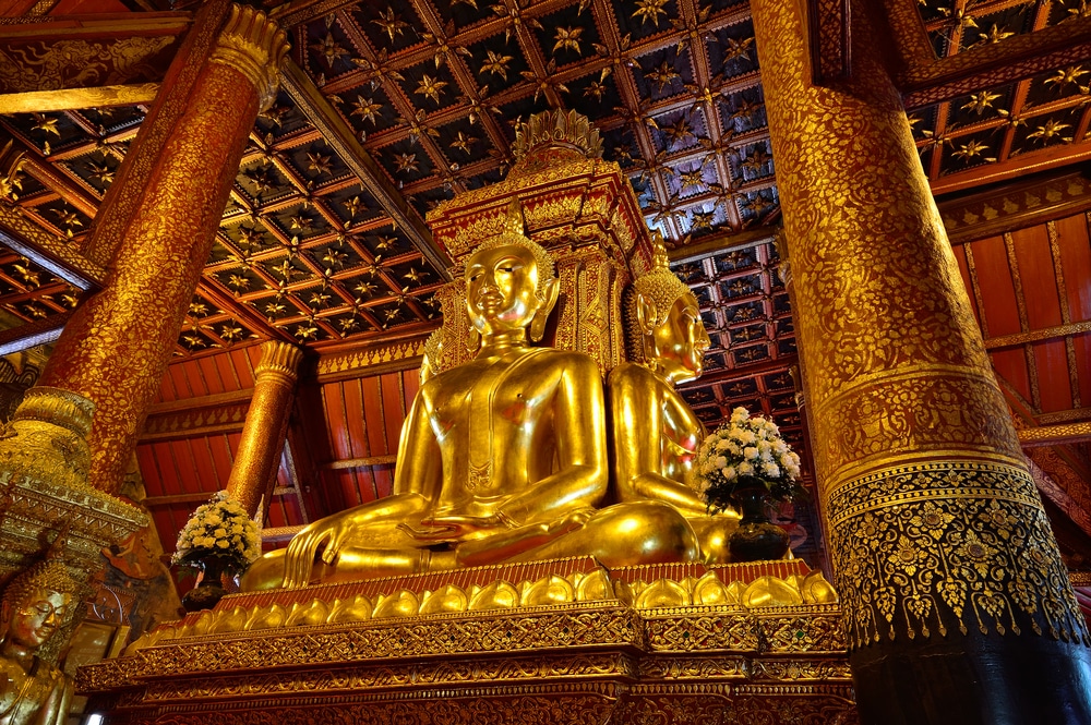 พระพุทธรูปทองขนาดใหญ่ที่นั่งหันหลังชนกันภายในวัดที่ตกแต่งอย่างวิจิตรด้วยเสาที่ประดับประดาด้วยลวดลายสวยงาม การจัดดอกไม้ และเพดานไม้ที่สลักลวดลายอย่างประณีต — นี่คือหนึ่งในสถานที่ท่องเที่ยวในน่านที่ห้ามพลาดสำหรับใครก็ตามที่วางแผนจะเที่ยวน่านและสัมผัสกับมรดกทางวัฒนธรรมอันเป็นเอกลักษณ์ของเมืองนี้.