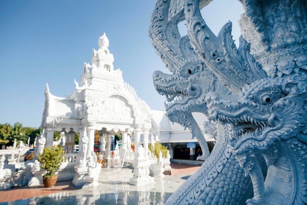 วัดสีขาวที่มีรูปปั้นมังกรลวดลายวิจิตรอยู่ด้านหน้า ท่ามกลางท้องฟ้าสีฟ้าใส—เป็นจุดท่องเที่ยวที่โด่งดังสำหรับใครก็ตามที่ต้องการเที่ยวเมืองน่าน หรือค้นพบสถานที่ท่องเที่ยวที่ไม่เหมือนใครในเมืองน่าน.