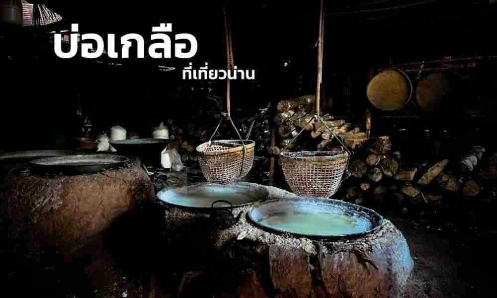 โรงงานผลิตเกลือที่มีตะกร้าสานสองใบแขวนอยู่เหนือหม้อดินเผาขนาดใหญ่ มีท่อนไม้เรียงซ้อนกันอยู่ด้านหลัง และมีข้อความภาษาไทยในมุมซ้ายบน; สถานที่ที่ไม่เหมือนใครแห่งนี้ถือเป็นจุดที่ต้องมาเยือนสำหรับผู้ที่กำลังสำรวจสถานที่ท่องเที่ยวในจังหวัดน่าน.