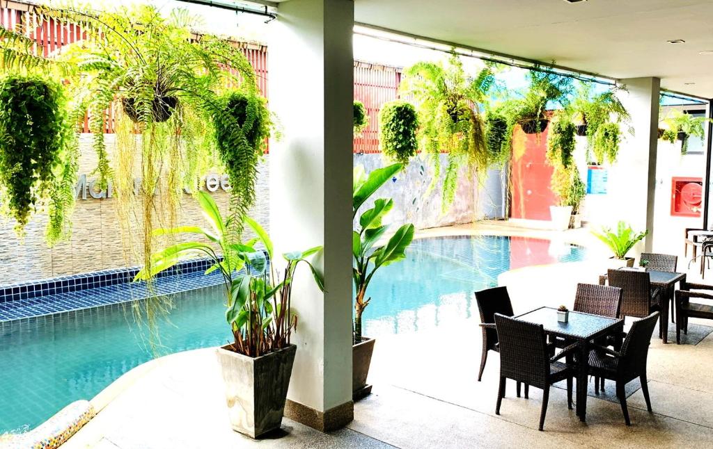 พื้นที่รับประทานอาหารกลางแจ้งที่มีโต๊ะและเก้าอี้ทำจากหวายสีดำ ตั้งอยู่ข้างสระว่ายน้ำที่ โรงแรมขอนแก่น ล้อมรอบด้วยต้นไม้ในกระถางและเฟิร์นแขวน พร้อมด้วยแสงแดดที่ส่องสว่างทั่วทั้งบริเวณ.