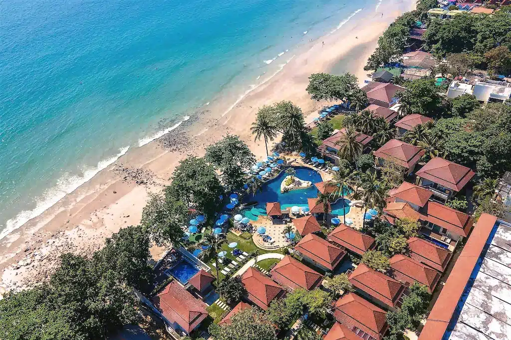 ภาพจากมุมสูงของรีสอร์ทริมชายหาดที่มีวิลลาหลังคาสีแดง สระว่ายน้ำ ต้นปาล์ม และชายหาดทรายขาวติดกับทะเลสีคราม — เป็นตัวเลือกที่สมบูรณ์แบบสำหรับผู้ที่กำลังมองหาที่พักเกาะช้างในสวรรค์เขตร้อน.