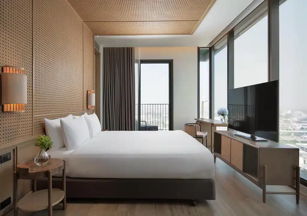 ห้องพักโรงแรมสไตล์ทันสมัย พร้อมด้วยเตียงขนาดใหญ่ โต๊ะข้างเตียง ทีวีจอแบน โต๊ะทำงาน และหน้าต่างสูงจากพื้นถึงเพดานที่มองเห็นวิวเมือง โทนสีกลางและการตกแต่งแบบมินิมัลช่วยสร้างบรรยากาศที่ผ่อนคลาย ทำให้โรงแรมขอนแก่นแห่งนี้กลายเป็นตัวเลือกที่สมบูรณ์แบบสำหรับทั้งนักเดินทางเพื่อธุรกิจและท่องเที่ยวที่ต้องการความสะดวกสบายในใจกลางเมือง.