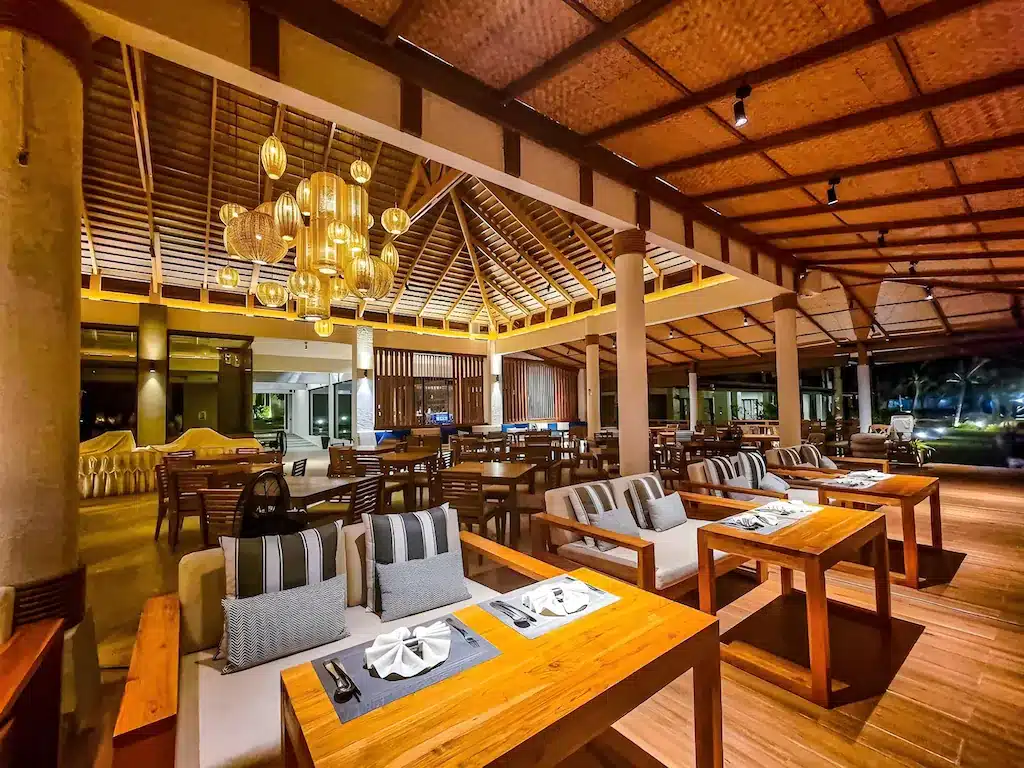 ภายในร้านอาหารที่กว้างขวาง พร้อมด้วยโต๊ะไม้ เก้าอี้มีเบาะนั่ง โคมไฟแขวนสไตล์โมเดิร์น และเพดานแบบเปิดโล่ง — เหมาะอย่างยิ่งสำหรับแขกที่ต้องการประสบการณ์การรับประทานอาหารอย่างมีสไตล์ระหว่างการเข้าพักที่ รีสอร์ทเกาะช้าง.