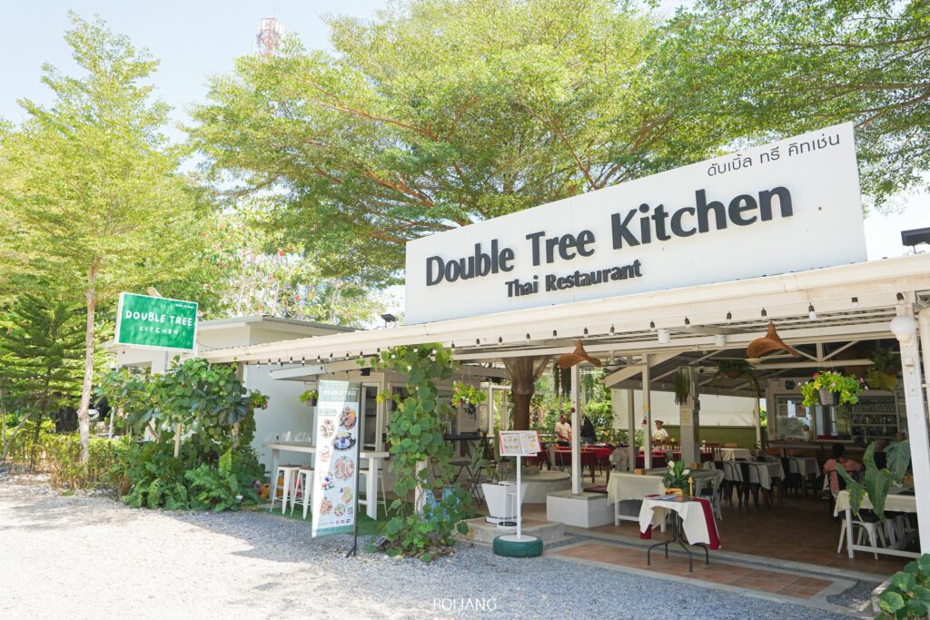 วิวกลางแจ้งของ Double Tree Kitchen ร้านอาหารเขาหลักพร้อมที่นั่งแบบเปิดโล่ง ต้นไม้เขียวขจี และป้ายทั้งภาษาอังกฤษและภาษาไทย.