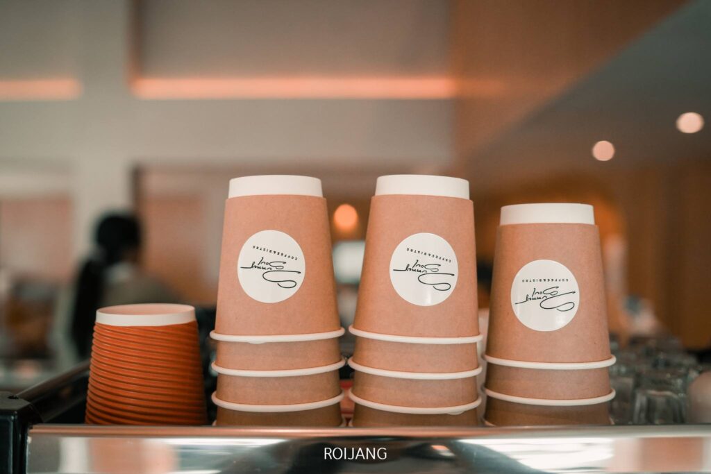 กองถ้วยกาแฟกระดาษพร้อมโลโก้วางอย่างประณีตบนเคาน์เตอร์ในร้านกาแฟ ร้านกาแฟภูเก็ต