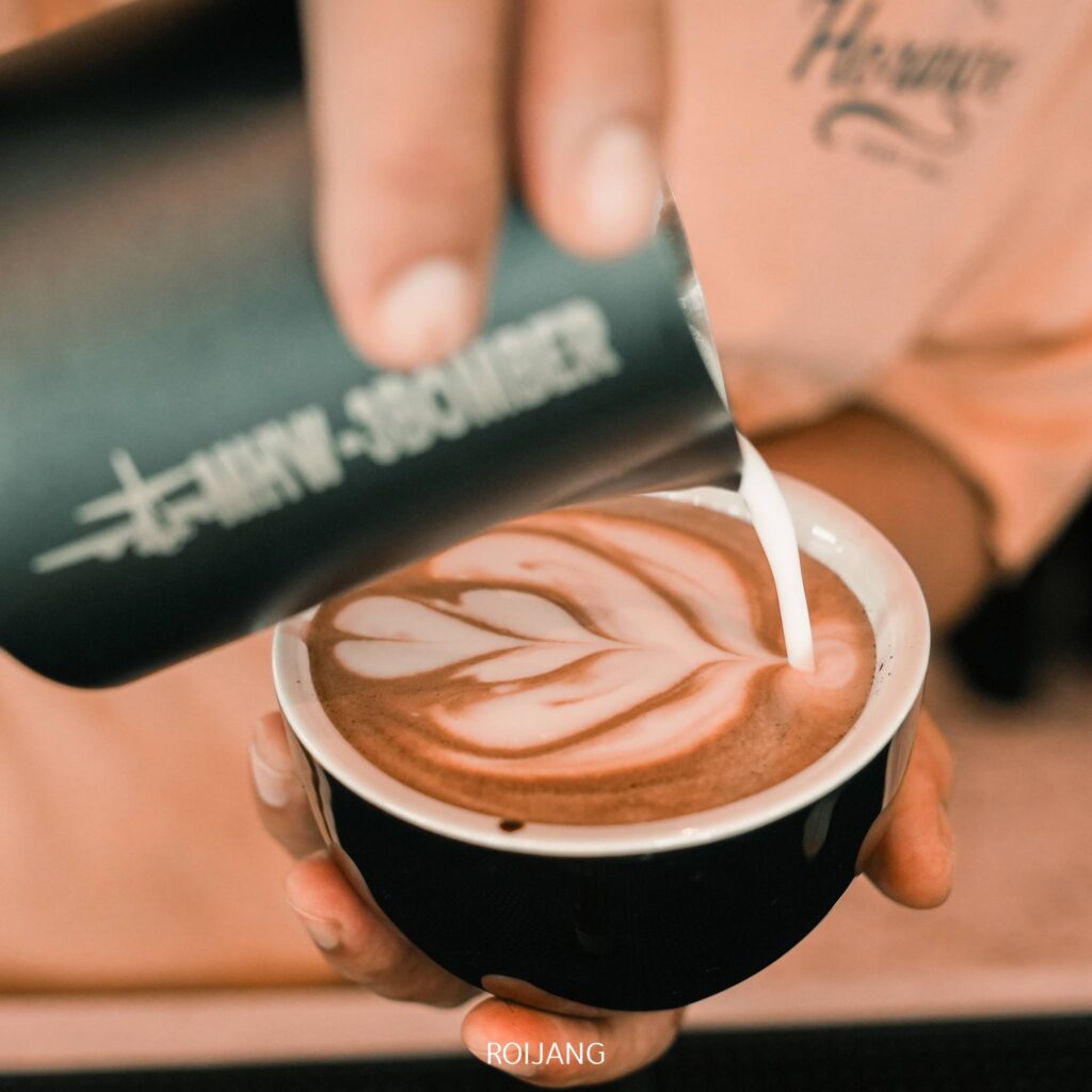 ภาพระยะใกล้ของบาริสต้าในร้านกาแฟ คาเฟ่ภูเก็ต  ภูเก็ตเทนมร้อนลงในกาแฟ ทำให้เกิดลาเต้อาร์ตที่มีลวดลายรูปหัวใจและใบไม้