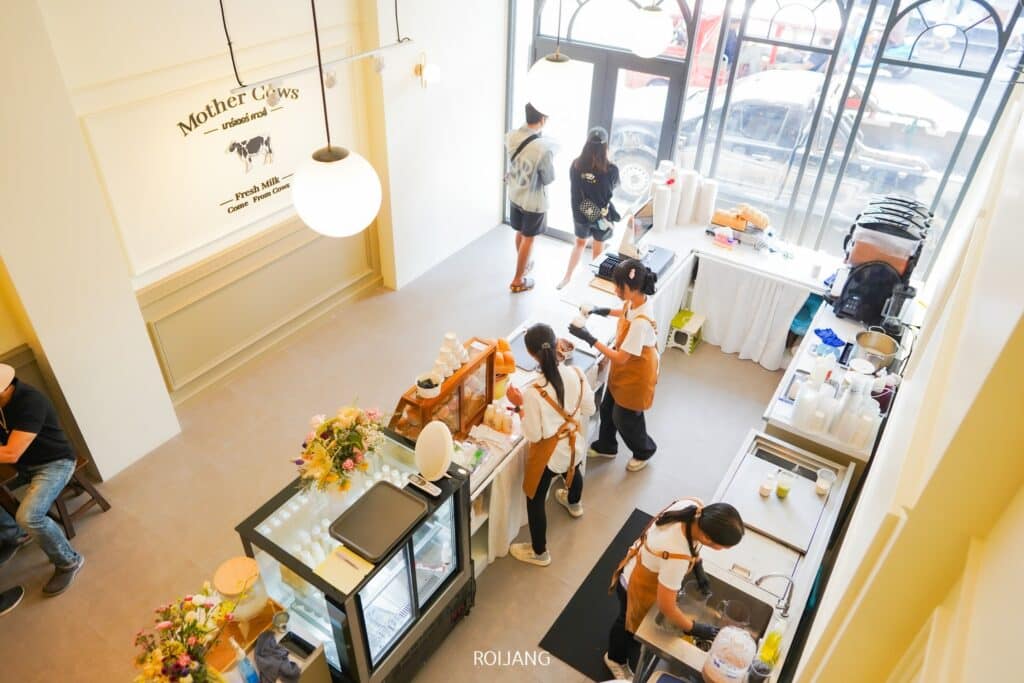 ภายในร้านกาแฟเต็มไปด้วยความคึกคักในขณะที่พนักงานกำลังเตรียมเครื่องดื่ม ผู้ชายคนหนึ่งยืนอยู่ที่เคาน์เตอร์ ในขณะที่อีกคนกำลังผ่อนคลายอยู่ใกล้ๆ หน้าต่างที่สว่างสดใสและการจัดดอกไม้สร้างบรรยากาศที่อบอุ่นใน ร้านกาแฟภูเก็ต ที่มีเสน่ห์แห่งนี้.