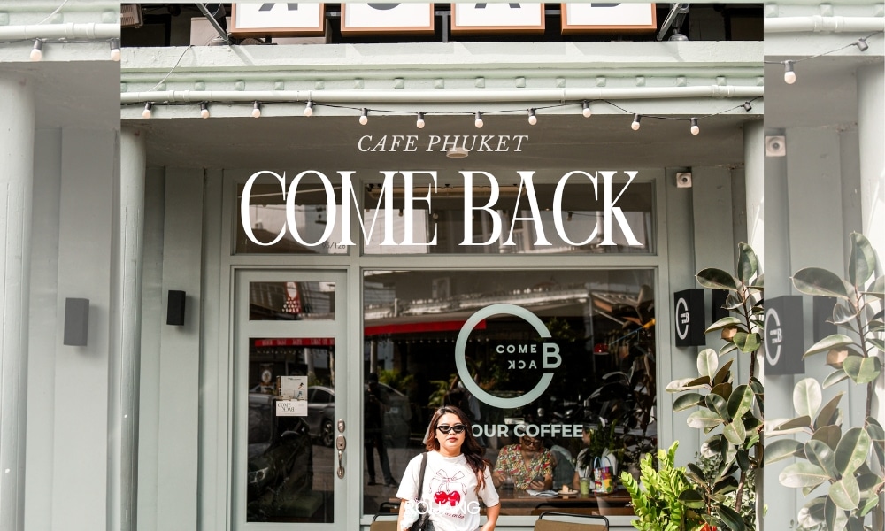 คนยืนอยู่หน้า “COME BACK” คาเฟ่ภูเก็ตสุดเก๋ที่ คาเฟ่ภูเก็ต มีด้านหน้าที่ทันสมัยด้วยต้นไม้เขียวชอุ่มและประตูกระจกที่ทันสมัย.