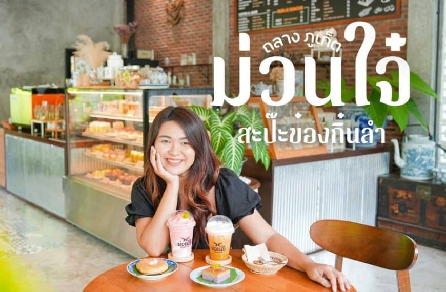 ผู้หญิงคนหนึ่งยิ้มขณะนั่งที่โต๊ะคาเฟ่ในคาเฟ่ภูเก็ต พลางจิบเครื่องดื่มและกินโดนัท ตู้โชว์และต้นไม้เขียวชอุ่มช่วยเติมเต็มบรรยากาศอบอุ่นเบื้องหลัง.