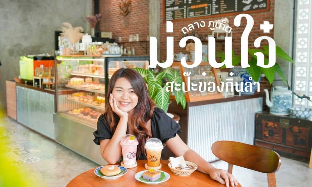 ผู้หญิงคนหนึ่งยิ้มขณะนั่งที่โต๊ะคาเฟ่ในคาเฟ่ภูเก็ต พลางจิบเครื่องดื่มและกินโดนัท ตู้โชว์และต้นไม้เขียวชอุ่มช่วยเติมเต็มบรรยากาศอบอุ่นเบื้องหลัง.