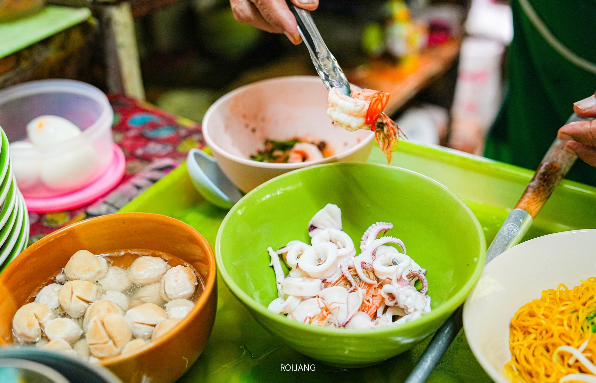 ในร้านอาหารตะกั่วป่าบรรยากาศ ร้านอาหารตะกั่วป่า สบายๆ ผู้คนจะเตรียมอาหารจานอร่อยอย่างเชี่ยวชาญโดยผสมผสานอาหารทะเลสด เส้นหมี่นุ่ม และลูกชิ้นรสเผ็ดในชามที่จัดอย่างสวยงาม.