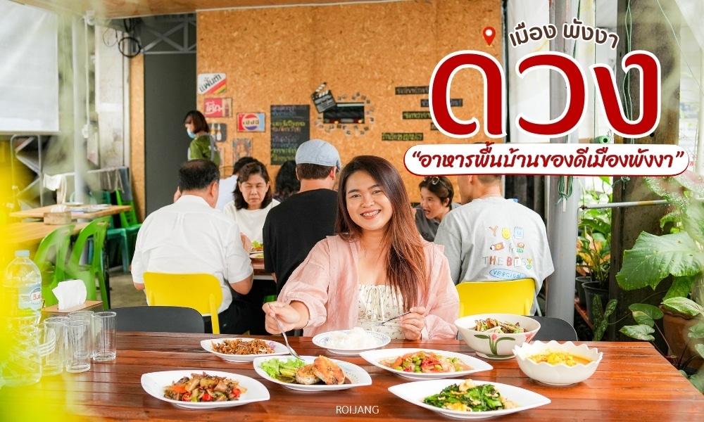 ผู้หญิงคนหนึ่งนั่งอยู่ ร้านอาหารพังงา ที่โต๊ะที่เต็มไปด้วยอาหารไทยรสเลิศจากร้านอาหารเมืองพังงา ยิ้มอย่างอบอุ่น ผู้ที่มารับประทานอาหารคนอื่นๆ จะเพลิดเพลินกับมื้ออาหารเป็นฉากหลัง ซึ่งช่วยเพิ่มบรรยากาศที่มีชีวิตชีวา ข้อความภาษาไทยซ้อนทับฉากอย่างหรูหรา