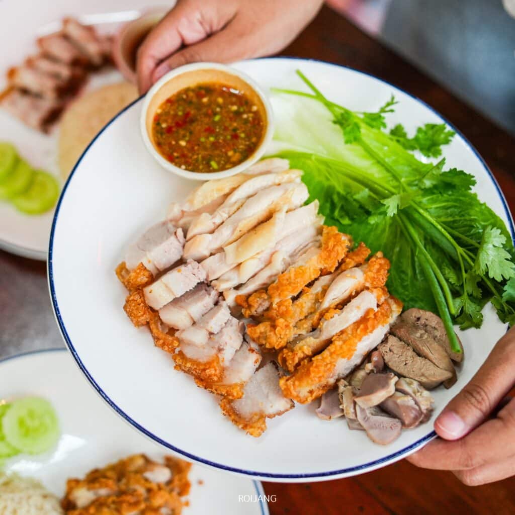 จานจาก ร้านอาหารภูเก็ต ประกอบด้วยหมูย่างและทอด ไก่ ผักใบเขียว น้ำจิ้มชามเล็ก ตับไก่และกึ๋น มือจับจาน. เหมาะสำหรับผู้ที่อยากลิ้มลองรสชาติต้นตำรับที่ ชาบูคอง ภูเก็ต