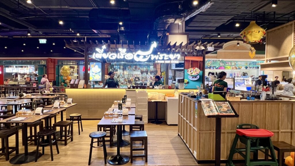 การตกแต่งภายในร้านอาหารสไตล์โมเดิร์นที่ร้านอาหารเซ็นทรัลภูเก็ต โดยมีป้ายไฟนีออนเขียนว่า "ลาวาและวิสตัน" พื้นที่รับประทานอาหารมีโต๊ะและเก้าอี้ไม้ ในขณะที่เคาน์เตอร์มีพนักงานที่สุภาพสองคนดูแล.