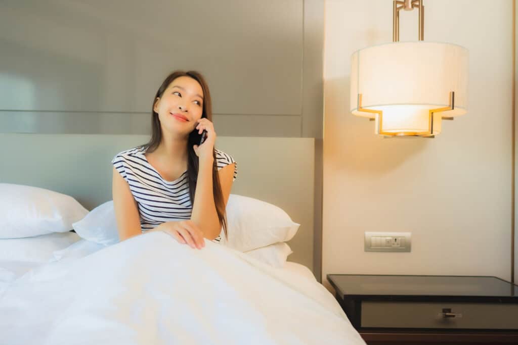 ผู้หญิงกำลังนั่งคุยโทรศัพท์อยู่บนเตียง โรงแรมลาดกระบัง