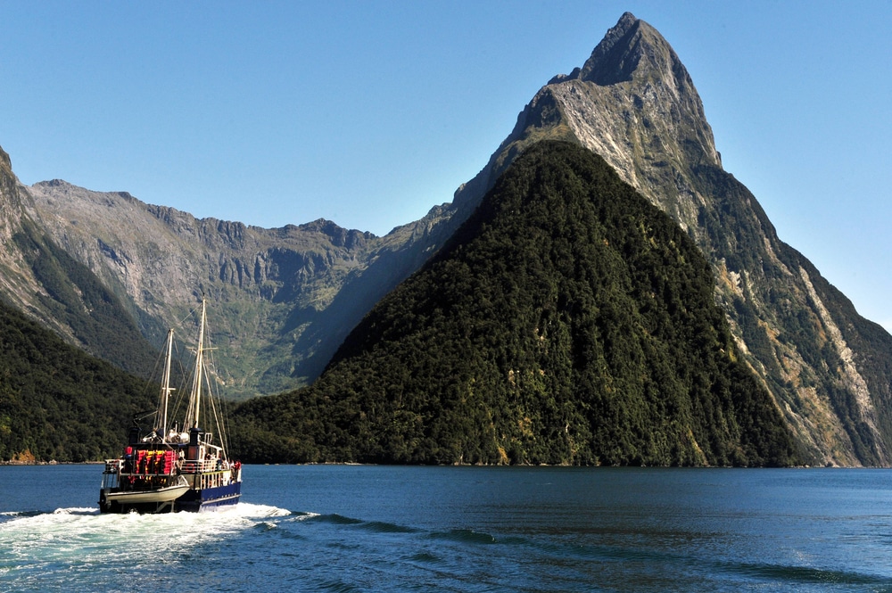 เรือแล่น ที่เที่ยวนิวซีแลนด์ ผ่านผืนน้ำโดยมีภูเขาเป็นฉากหลัง