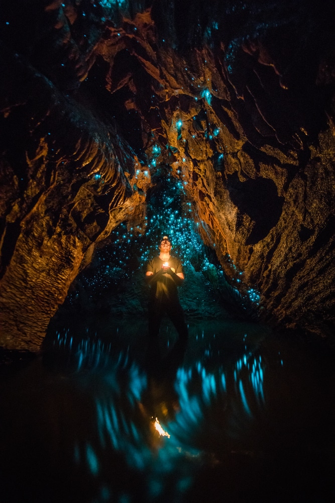 ชาย ที่เที่ยวนิวซีแลนด์ คนหนึ่งยืนอยู่ในถ้ำที่มีแสงเรืองรอง
