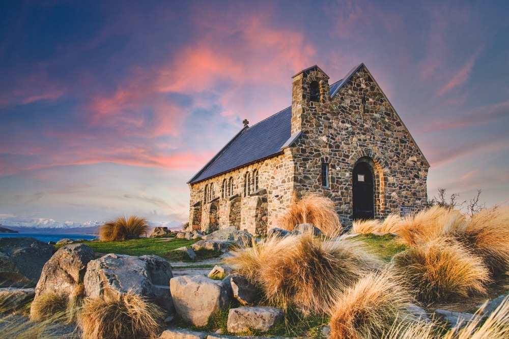 โบสถ์ สถานที่ท่องเที่ยวนิวซีแลนด์ บนเนินเขาที่มีหญ้าและหินอยู่ข้างหน้า