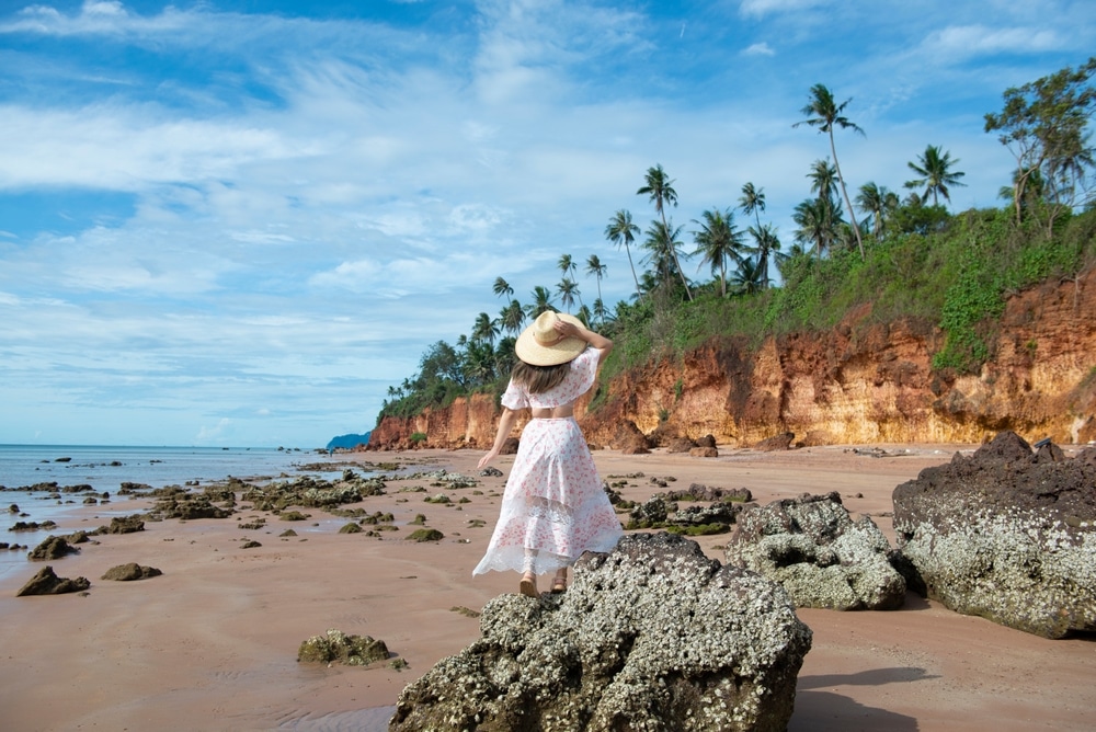 ผู้หญิงใน เที่ยวบางสะพาน ชุดสีขาวและหมวกฟางยืนอยู่บนชายหาด