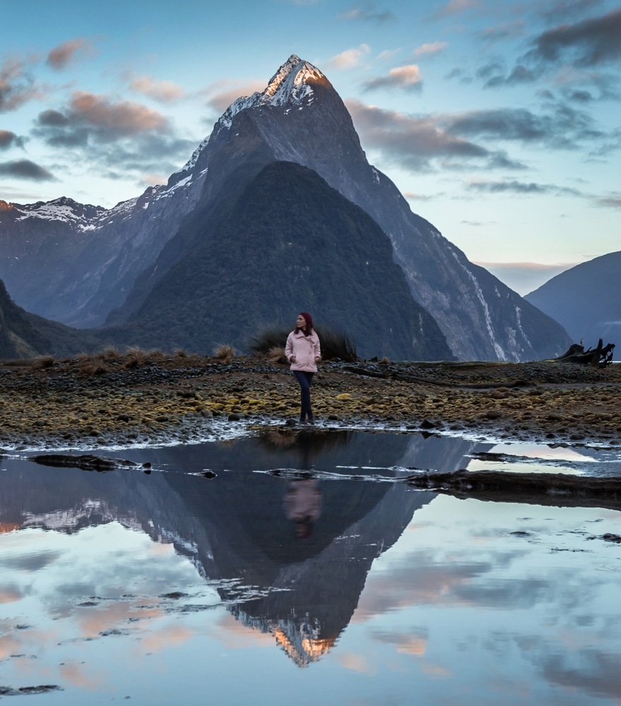 คนที่ยืน ที่เที่ยวนิวซีแลนด์ อยู่ในทุ่งที่มีภูเขาอยู่เบื้องหลัง