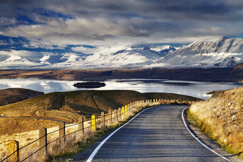 ถนนยาว เที่ยวนิวซีแลนด์ ที่มีรั้วและภูเขาเป็นฉากหลัง