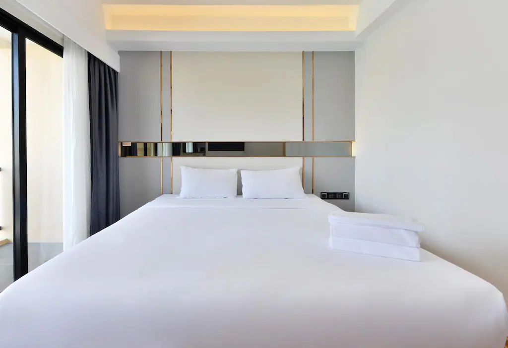 เตียงสีขาวขนาดใหญ่นั่งอยู่ในห้องนอนข้างหน้าต่าง รีสอร์ทใกล้สนามบินสุวรรณภูมิ