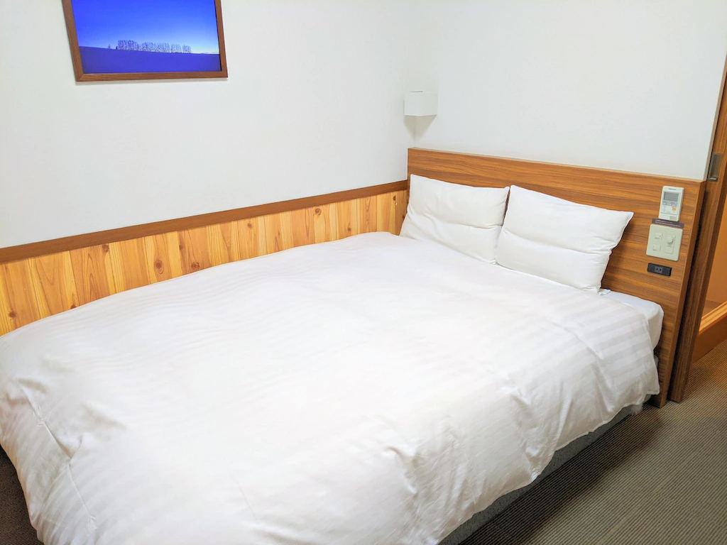 เตียง เที่ยวฮอกไกโด สีขาวนั่งอยู่ในห้องนอนข้างหัวเตียงไม้