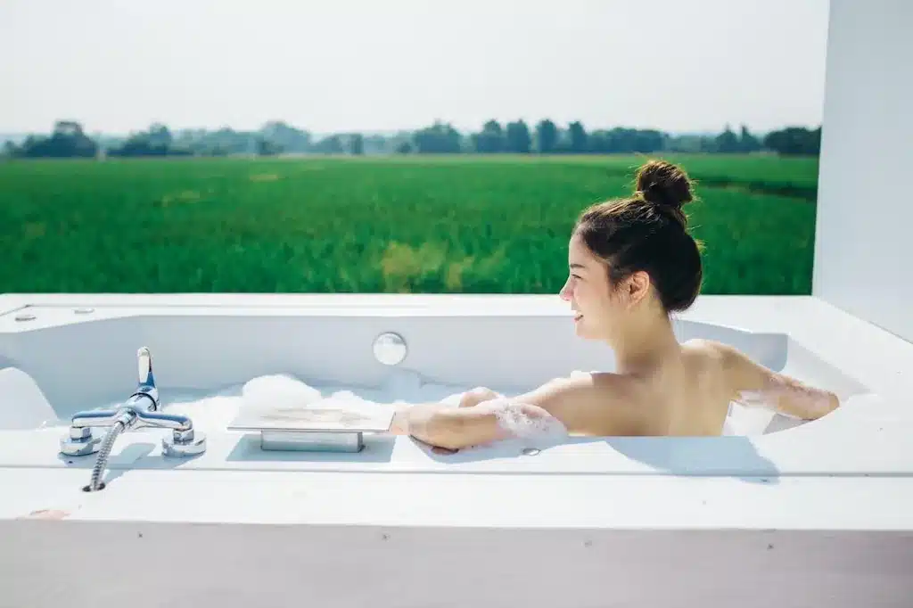 ผู้หญิงนั่ง ที่พักฝาง อยู่ในอ่างอาบน้ำโดยมีทุ่งหญ้าเขียวขจีเป็นฉากหลัง