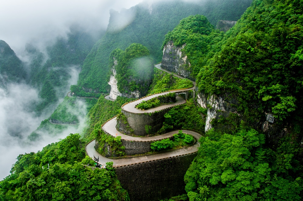 ถนนคดเคี้ยวบน เที่ยวจีน ภูเขาที่โอบล้อมด้วยต้นไม้เขียวขจี