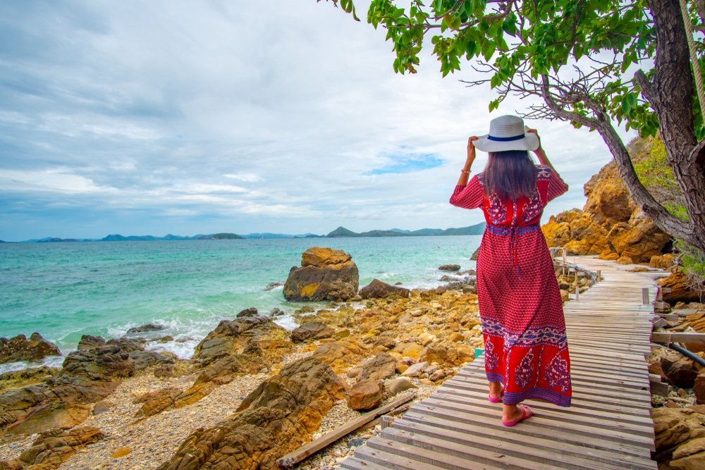 ธรรมชาติใกล้กรุงเทพ ผู้หญิงสวมชุดสีแดงและหมวกเดินไปตามทางเดินไม้ใกล้ทะเล เพลิดเพลินกับธรรมชาติใกล้กรุงเทพฯ