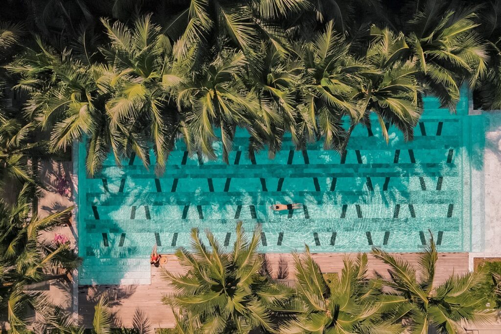 ภาพมุมสูงของสระว่ายน้ำที่ล้อมรอบด้วยต้นปาล์มที่แหลมพรหมเทพ พระอาทิตย์ตกแหลมพรหมเทพ