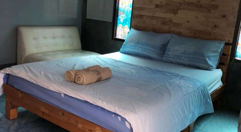 เตียงไม้หัวเตียงปูด้วยผ้าปูที่นอนสีฟ้า ณ ที่พักริมแม่น้ำในราชบุรี
