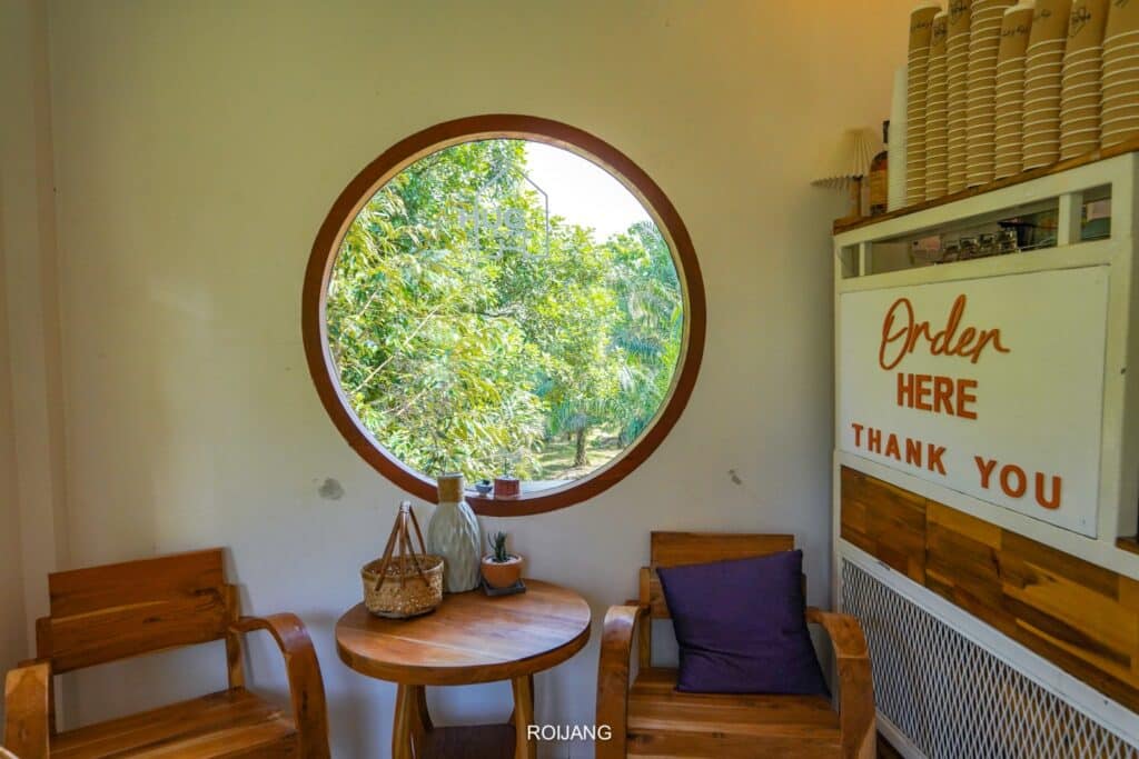 หน้าต่างกลมๆ ในห้องเล็กๆ กับโต๊ะและเก้าอี้ที่คาเฟ่พังงา ร้านกาแฟพังงา
