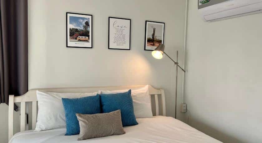 เตียงสีขาวและหมอนสีน้ำเงินในห้องนอนที่เกสต์เฮ้าส์ริมน้ำในจังหวัดราชบุรีสำหรับนักเดินทาง