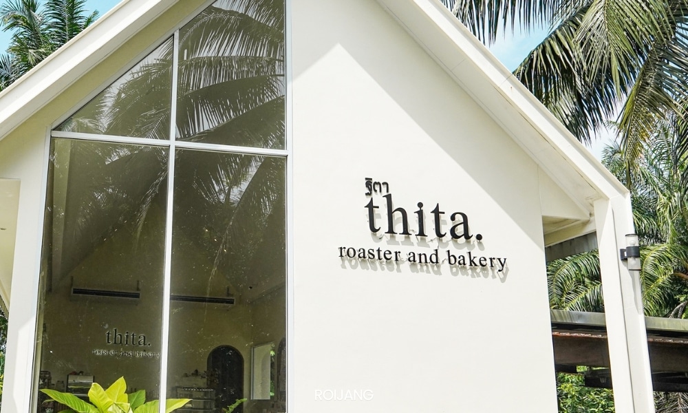 ภายนอก คาเฟ่พังงา อาคารสีขาวมีหน้าต่างบานใหญ่ มีป้าย “thita. roaster and bakery” รายล้อมไปด้วยต้นปาล์มที่โอนเอน ทำให้เป็นร้านกาแฟพังงาที่มีเสน่ห์.