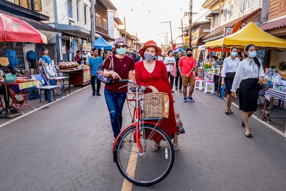 ผู้หญิงสวมหน้ากากขี่จักรยานไปตามถนนในจังหวัดราชบุรี สถานที่ท่องเที่ยวยอดนิยมของประเทศไทย เที่ยวเขมราฐ