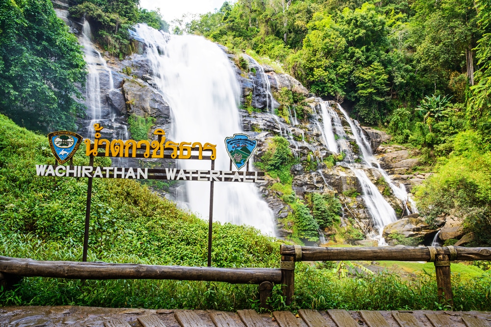 น้ำตกที่มีรั้วไม้และมีป้ายชื่ออยู่ข้างหน้า กาญจนบุรี หนึ่งในจุดหมายปลายทางยอดนิยมของการท่องเที่ยวในประเทศไทย น้ำตกเชียงใหม่สวยๆ